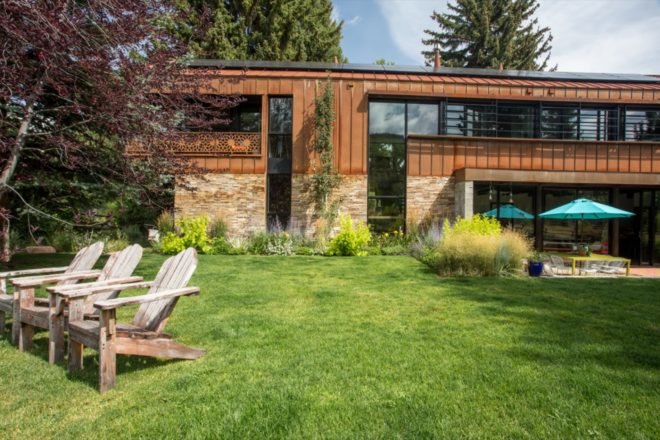 wood lounge chairs in yard outside of home with weathered steel siding