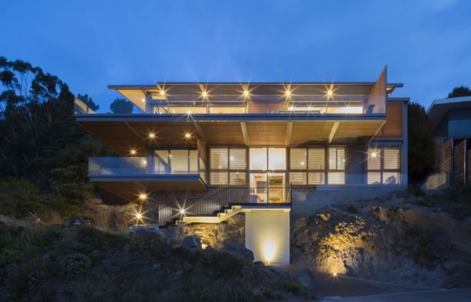 stone home with timber slat screens over large glass windows at night