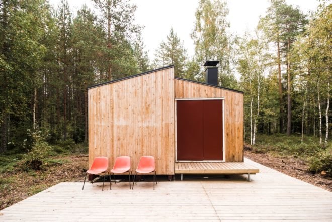 side view of wooden cabin with large wood deck with three red seats