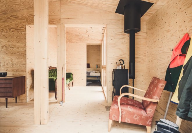 interior of wood-lined cabin with wood-burning fireplace and red chair