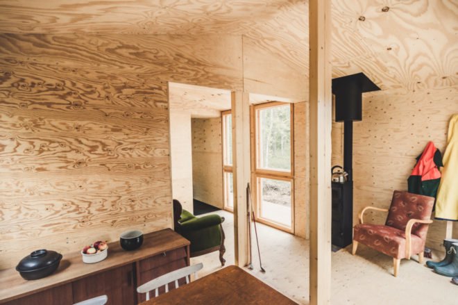 room with wood walls, ceilings and floors plus a black wood-burning fireplace next to a red chair