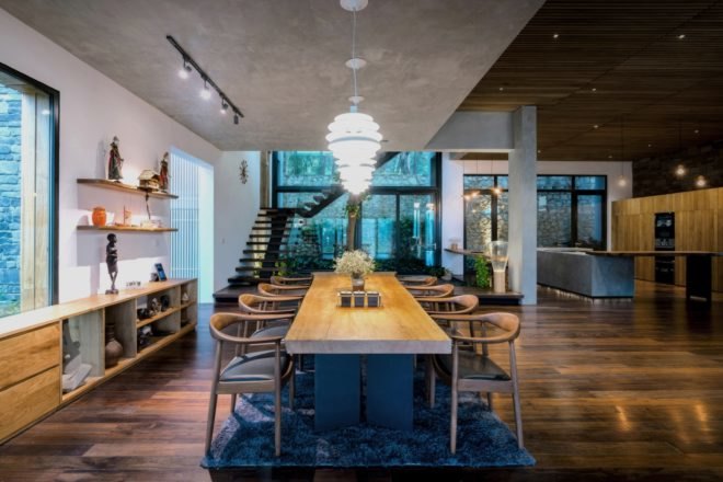 long wood dining table and chairs on a plush rug under hanging lamps