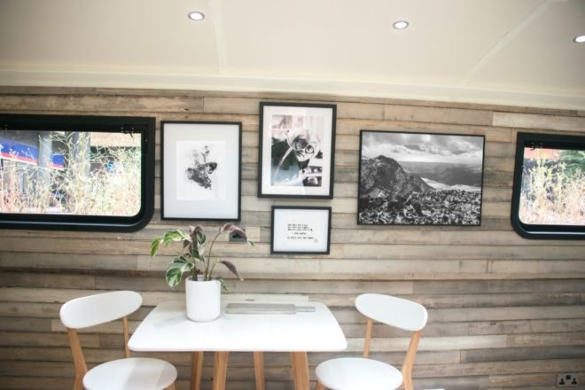Small dining table and chairs with potted plant on table and framed photographs on wood-lined wall