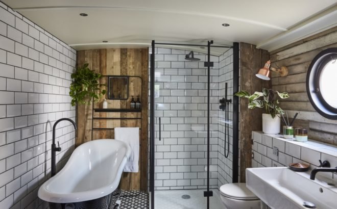 bathroom with white subway tiles, wood accent walls, standalone bathtub, glass shower, and potted and hanging plants