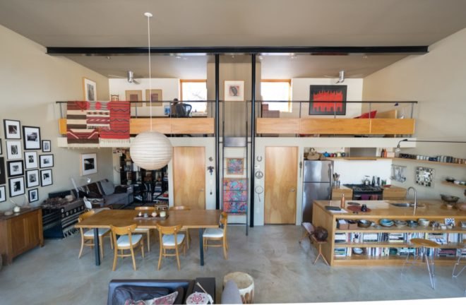 open-plan living area with light wood dining table and kitchen island below lofted bedroom