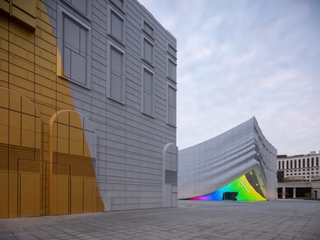 white and gold building near white warped building with a rainbow-colored, mirrored entrance