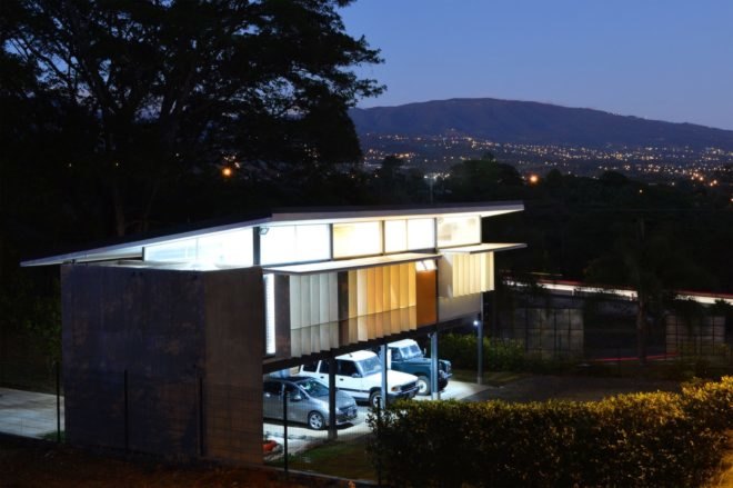 home on stilts with open solar shades at night