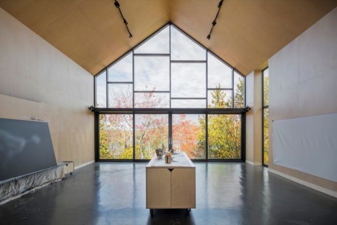 large room with pitched roof, timber walls, shiny concrete floors and a glass wall facing forest and lake
