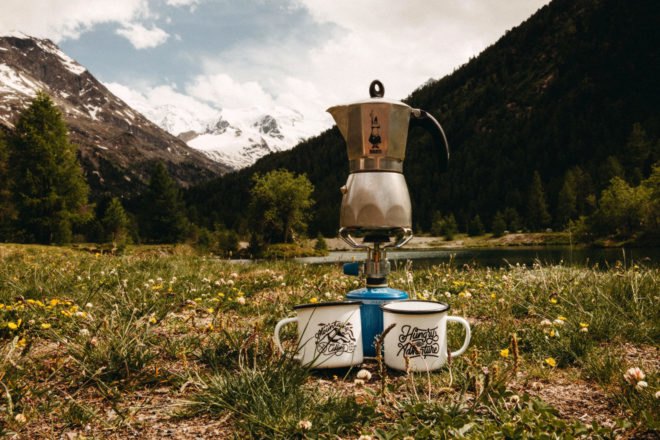 metal kettle on a cookstove with mugs nearby in front of mountainous landscape