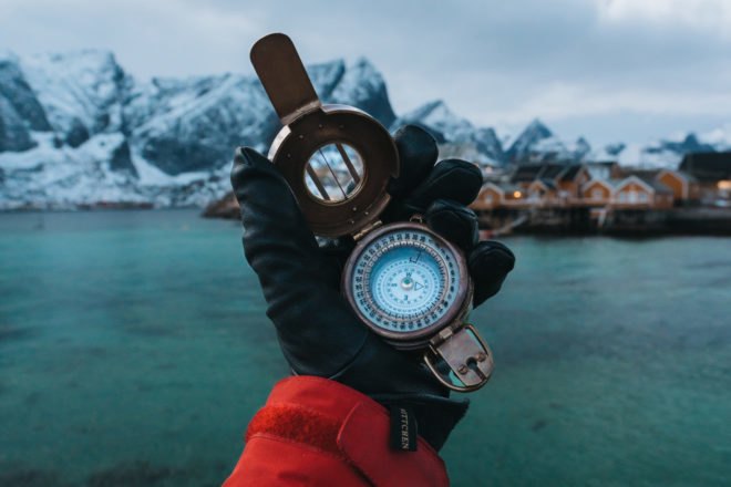 Gloved hand holding a compass with snow-covered mountains in the background