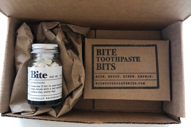 Glass jar of toothpaste tablets and small cardboard box in a larger, open cardboard box