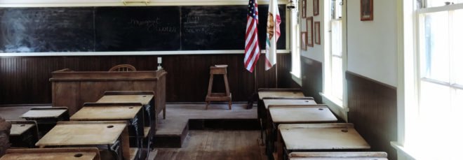 cropped close-up of Empty classroom with wooden desks, wooden teacher desk at front of room and black chalkboard