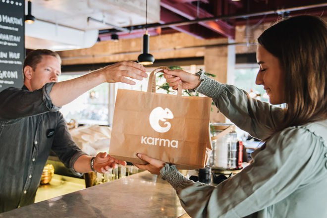 person picking up brown paper bag with karma logo on it from a restaurant
