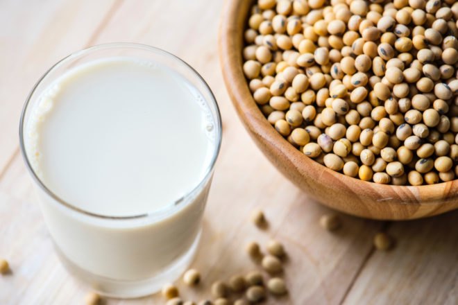 glass of soy milk next to a bowl of soy beans