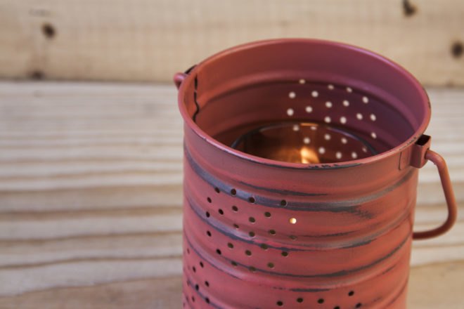 rust-red painted tin can with holes and a candle inside