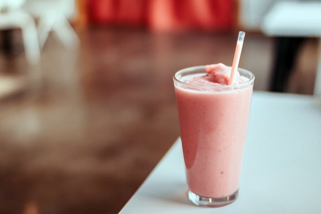strawberry milkshake in glass cup with plastic straw on a table
