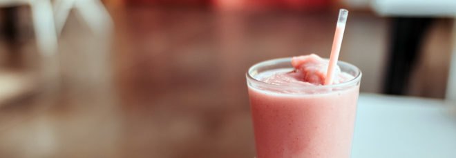 cropped close-up of strawberry milkshake in glass cup with plastic straw on a table