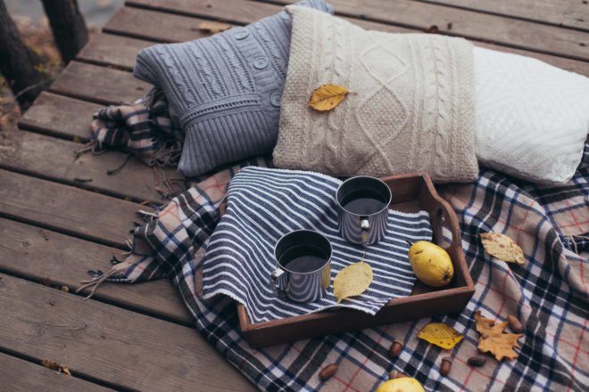 pillows with sweater covers, a blanket, and a tray with coffee on an outdoor deck