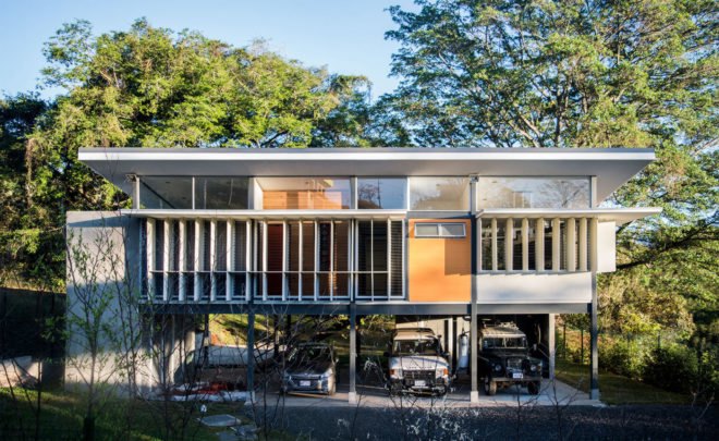 front of white home on stilts with solar shades over windows