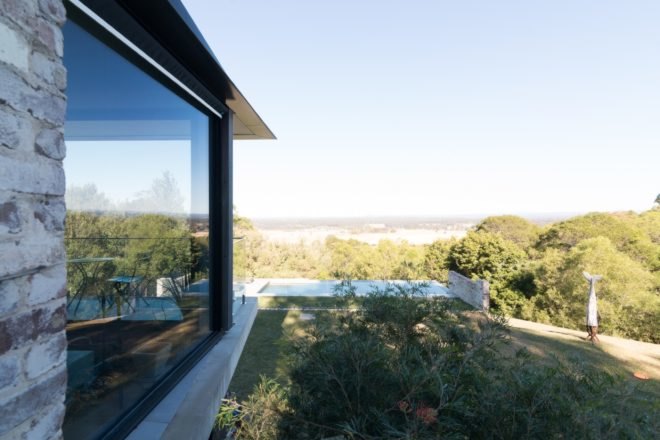 home with brick and glass wall facing forested landscape