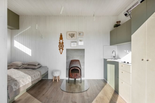 white room with bed, wood-burning stove and small kitchen