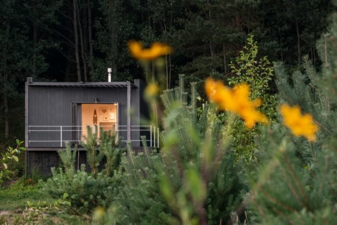 black hut surrounded by greenery with yellow flowers in foreground