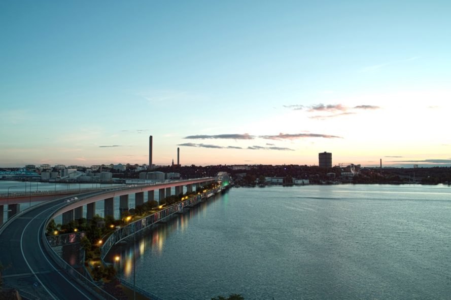 rendering of bridge with glass apartments below and a park on top leading to a city