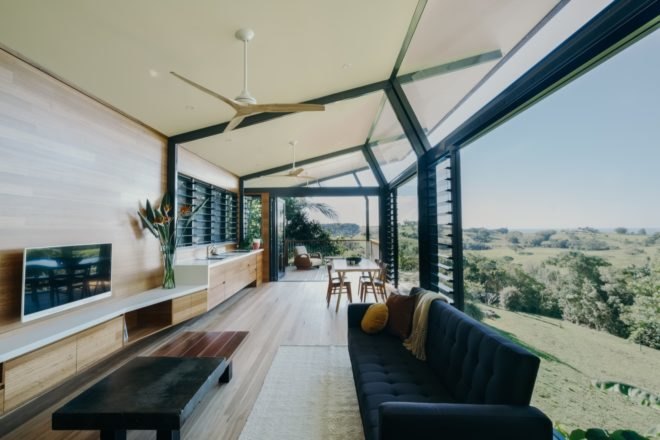 cabin with glass and timber walls with open plan living, dining and kitchen area