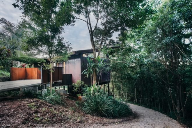 elevated glass and weathered steel cabin in a rainforest