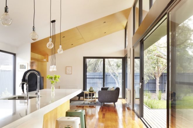 open-plan living room and kitchen with white walls and cabinets, wood floors, a gray couch and several large windows