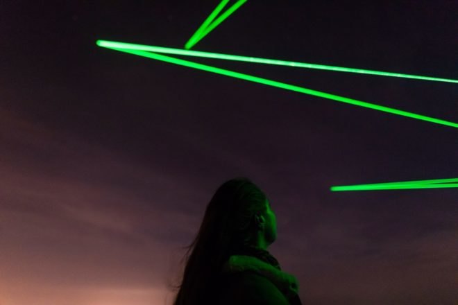 person looking up at green lights in dark sky