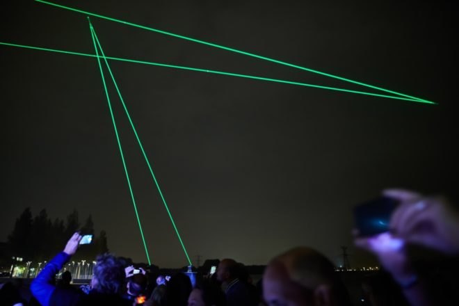 crowd looking up at green laser lights in dark sky