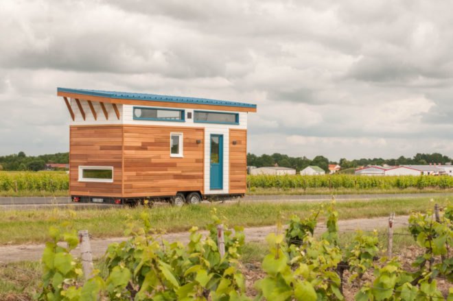tiny home clad in cedar panels with white trim and teal front door