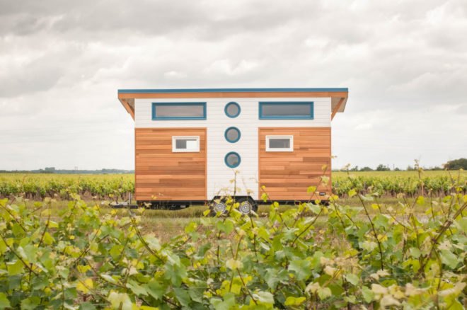 tiny home clad in cedar panels with white trim and blue-framed round windows