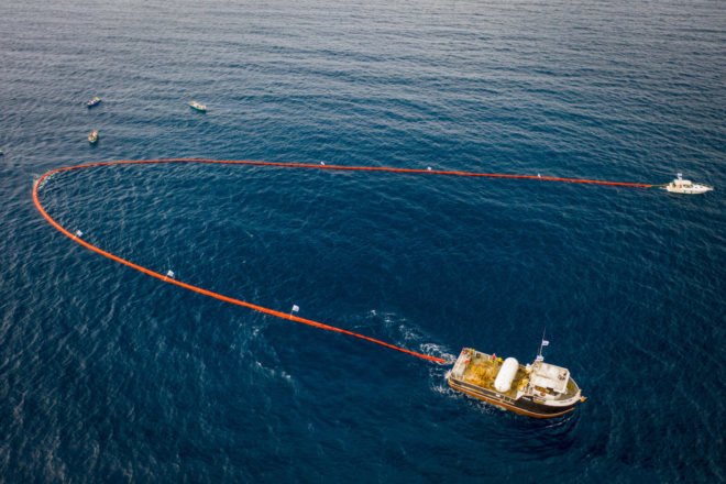 Two boats pulling an orange ocean sweeping device