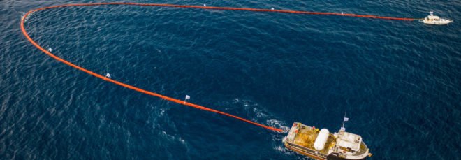 Two boats pulling an orange ocean sweeping device