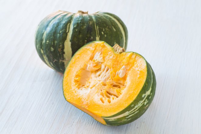 one whole green kabocha squash and half of a kobocha squash with yellow flesh and seeds showing