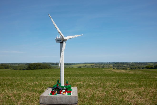 wind turbine above a cottage all made from LEGOS outside in vast green lot under blue skies