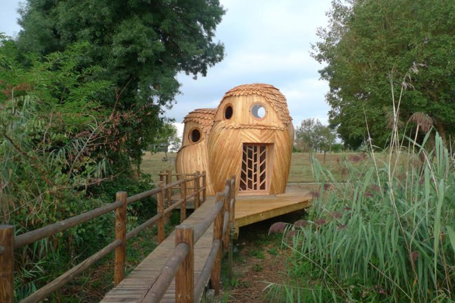 wood walkway leading to wood tiny home in the shape of two owls