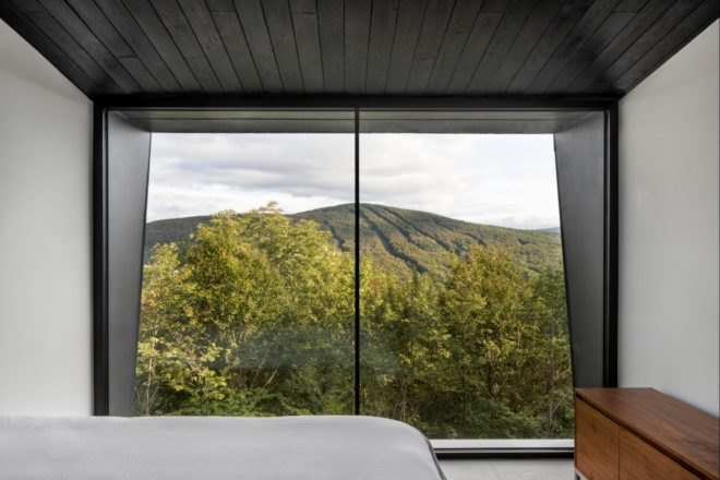 bedroom with glass window looking out over forest