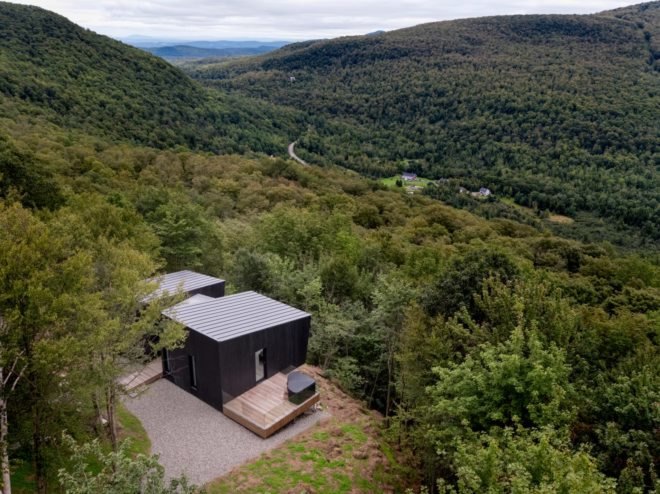 two black cabins connected by wood walkway surrounded by forest