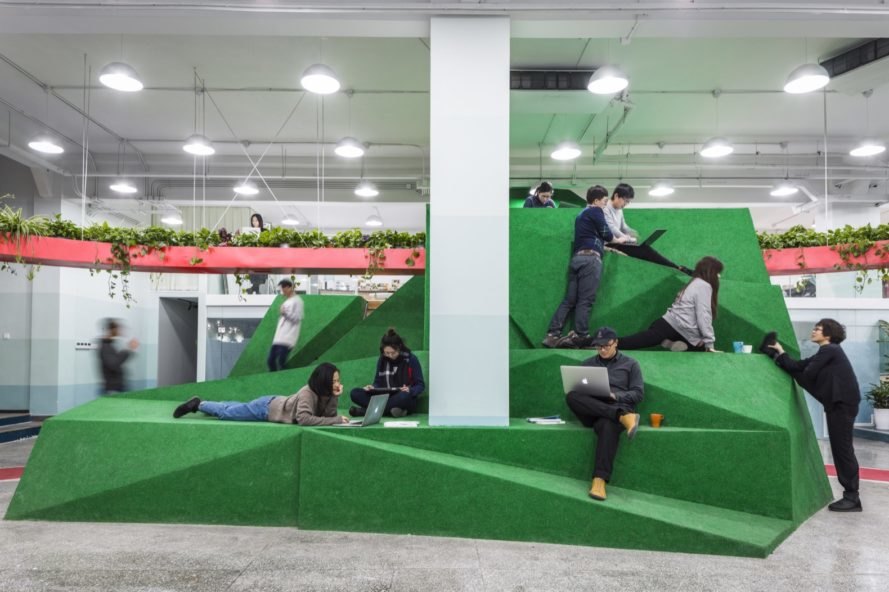 tall green geometric volume with people sitting, standing and lying on the structure