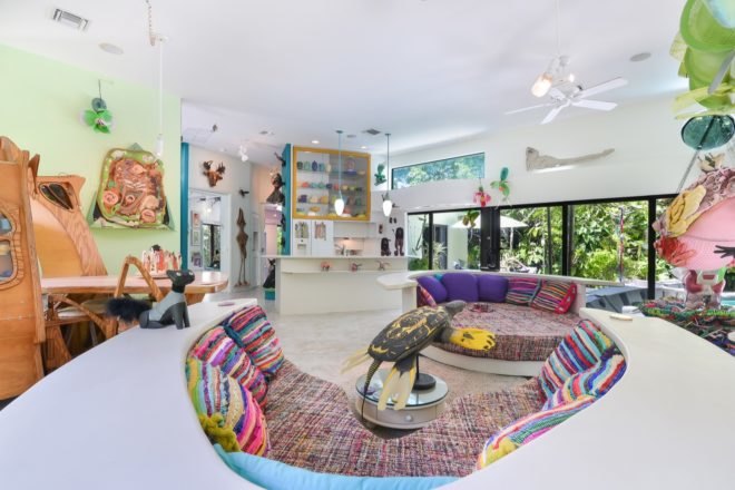 curving white couches facing a white kitchen filled with art and sculptures
