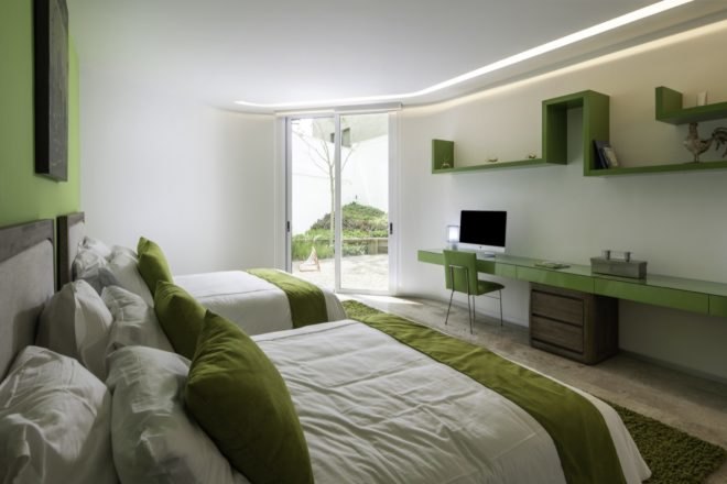 green and white bedroom with two double beds with white and green bedding and a long green desk