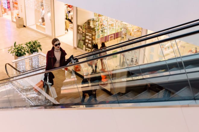 woman with shopping bags on escalator in mall