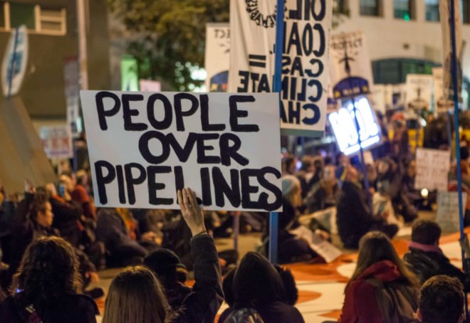 person holds a sign that reads, "People over pipelines"