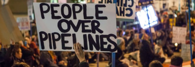 person holds a sign that reads, "People over pipelines"
