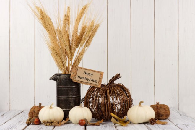 pumpkins, tin container of wheat, twig pumpkin and leaves on a white table