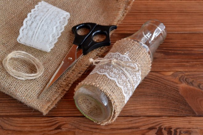 old glass bottle wrapped in burlap, lace and twine near pair of scissors