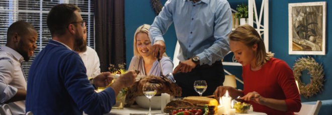 people around a dinner table talking while man carves turkey